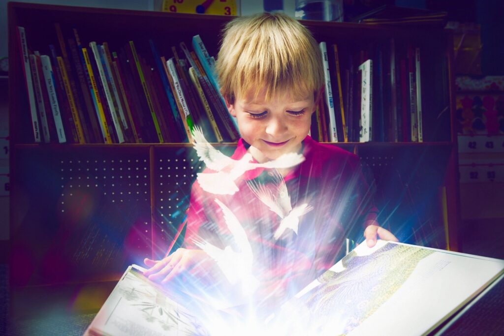 A young boy is reading a book with light coming from it.