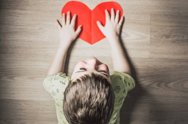 A boy is holding up a paper heart