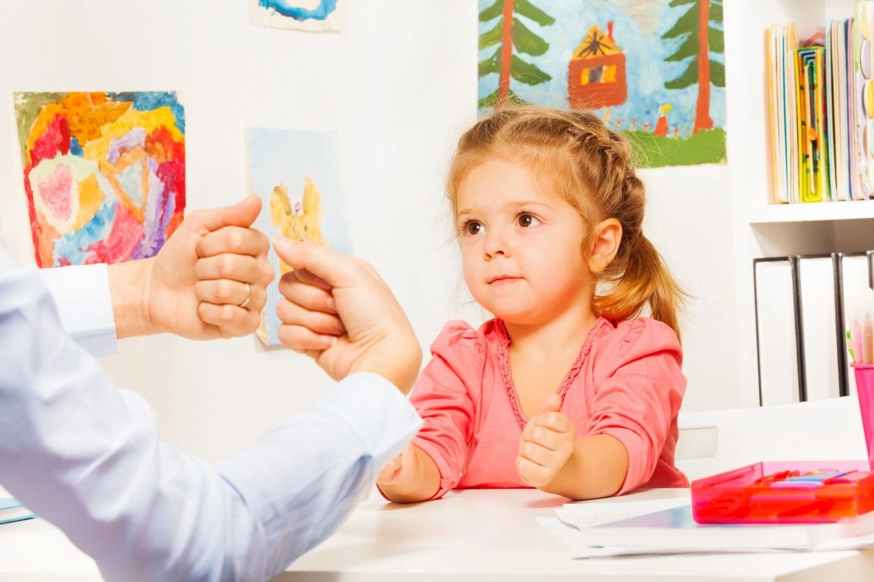 A little girl sitting at the table with an adult.