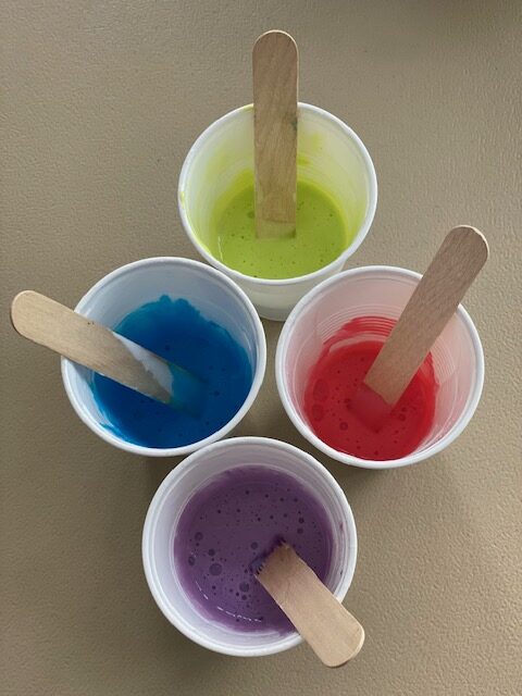 Four cups of different colors with wooden spoons in them.