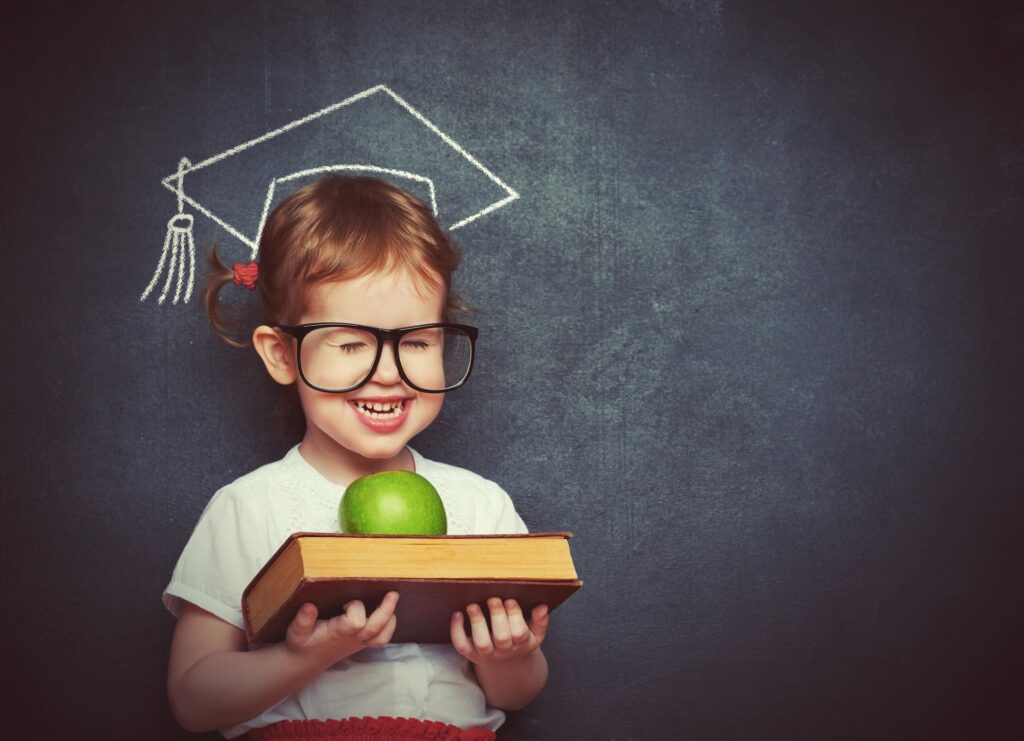 A little girl holding an apple and wearing glasses.